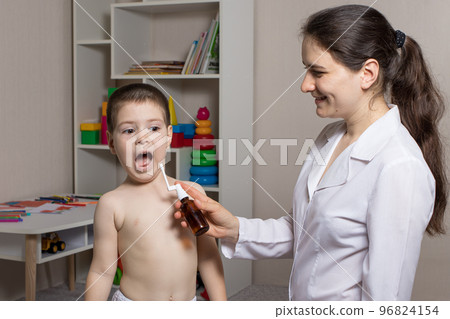 A pediatrician or nurse and a boy 3-4 years old. Throat spray, treatment of pharyngitis, stomatitis or thrush in children. 96824154
