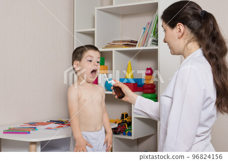 A pediatrician or nurse and a boy 3-4 years old. Throat spray, treatment of pharyngitis, stomatitis or thrush in children. A pediatrician or nurse and a boy 3-4 years old. Throat spray, treatment of pharyngitis, stomatitis or thrush in children. 96824156