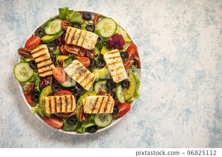 Greek style cuisine - salad with grilled halloumi cheese, avocado, pecan nuts and tomatoes. 96825112
