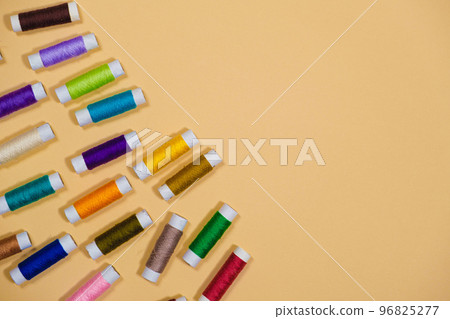 A set of multi-colored threads for sewing with an empty space for text on a beige background, top view. Tailoring and needlework equipment, tailor banner. A set of multi-colored threads for sewing with an empty space for text on a beige background, top view. Tailoring and needlework equipment, tailor banner. 96825277