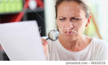 Woman with puzzled face reads document or recipe with magnifying glass in her hand. Woman with puzzled face reads document or recipe with magnifying glass in her hand. 96828538