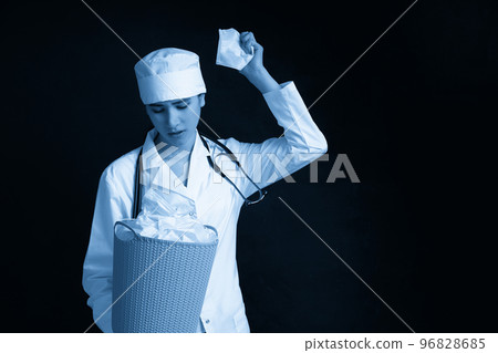 Doctor holding bucket full of used facial masks, throwing them away as symbol of epidemic ending Doctor holding bucket full of used facial masks, throwing them away as symbol of epidemic ending 96828685