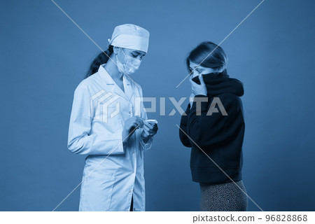 Young doctor measuring temperature of a patient with thermometer, studio shot on blue background Young doctor measuring temperature of a patient with thermometer, studio shot on blue background 96828868