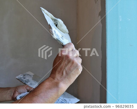formation of an even slope angle in the window opening by applying a layer of mortar with spatulas in the hands of the builder, plastering the window slope in the room formation of an even slope angle in the window opening by applying a layer of mortar with spatulas in the hands of the builder, plastering the window slope in the room 96829035