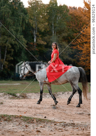 Riding a horse, walking in an autumn forest, a woman riding a horse in a long red dress with bare feet. 96829114