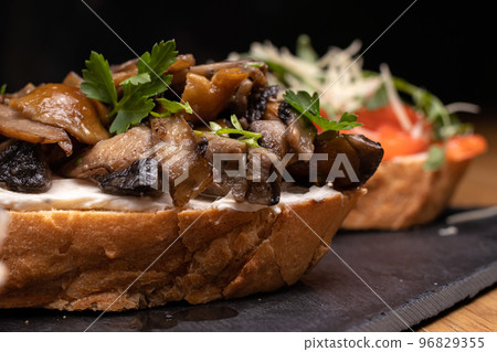 Bruschetta with mushrooms, soft cheese and herbs on a black background. Delicious sandwiches and snacks. Bruschetta with mushrooms, soft cheese and herbs on a black background. Delicious sandwiches and snacks. 96829355