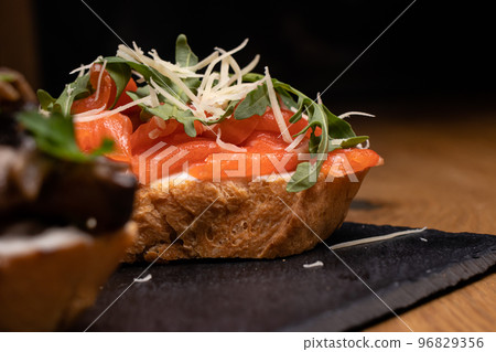 Bruschetta from a French loaf with salmon, cheese and arugula. Snacks and sandwiches Bruschetta from a French loaf with salmon, cheese and arugula. Snacks and sandwiches 96829356