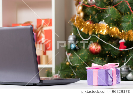 Laptop near the Christmas tree. Buying gifts and congratulations online via the Internet. 96829378