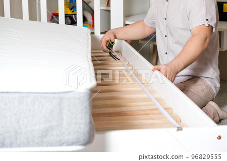 A man assembles a children's bed, measures the length with a tape measure, hands close-up. A man assembles a children's bed, measures the length with a tape measure, hands close-up. 96829555