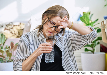 Mature woman suffering from headache, at home with glass of water 96829782