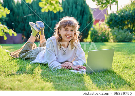 Teenage girl lying on grass using laptop, looking at camera 96829790