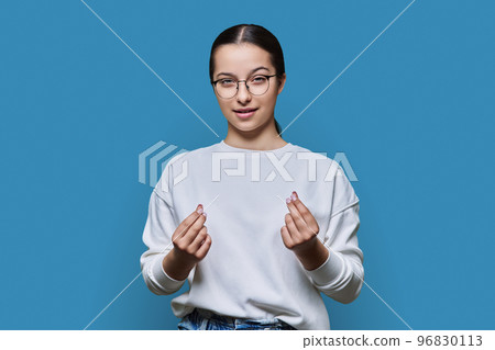 Teenage girl making money gesture, rubbing her fingers, on blue background 96830113