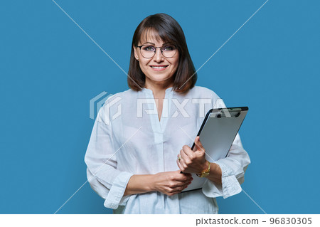 Middle aged business woman with clipboard looking at camera on blue background 96830305