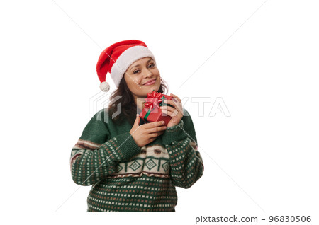 Attractive multi-ethnic woman in Santa hat and warm green sweater, holding Christmas present near her face, smiling cutely looking at camera, isolated over white background with free advertising space Attractive multi-ethnic woman in Santa hat and warm green sweater, holding Christmas present near her face, smiling cutely looking at camera, isolated over white background with free advertising space 96830506