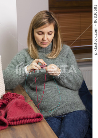 Beautiful pregnant women knits sitting in chair, wears warm clothes,sweater in cold season. Hobby, activity.Red ball of yarn, thread lays on table. Horizontal Beautiful pregnant women knits sitting in chair, wears warm clothes,sweater in cold season. Hobby, activity.Red ball of yarn, thread lays on table. Horizontal 96830693