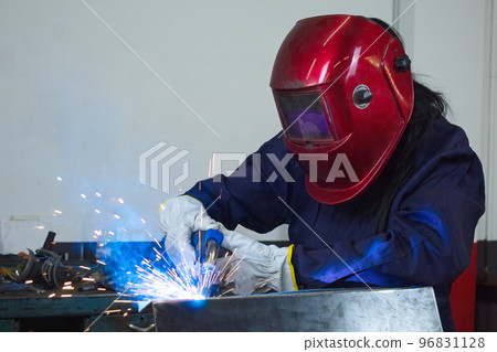 worker woman with gloves working in a workshop welding metal with helmet and overalls worker woman with gloves working in a workshop welding metal with helmet and overalls 96831128