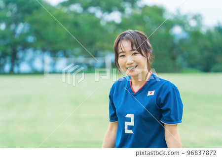 A Japanese woman of a smiling fan, supporter, and player standing on a futsal/soccer field A Japanese woman of a smiling fan, supporter, and player standing on a futsal/soccer field 96837872