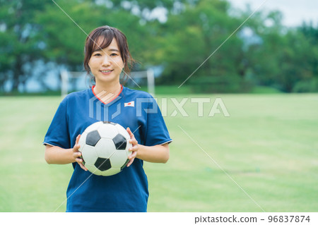 A Japanese woman who is a smiling fan, supporter, and player standing on a futsal soccer field while holding a soccer ball A Japanese woman who is a smiling fan, supporter, and player standing on a futsal soccer field while holding a soccer ball 96837874