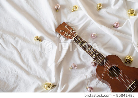 Ukulele guitar, Christmas balls and garland lights on white. Winter festive composition. Ukulele guitar, Christmas balls and garland lights on white. Winter festive composition. 96841485