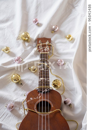 Ukulele guitar, Christmas balls and garland lights on white. Winter festive composition. Ukulele guitar, Christmas balls and garland lights on white. Winter festive composition. 96841486
