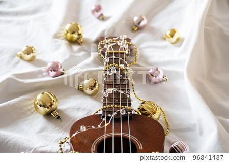 Ukulele guitar, Christmas balls and garland lights on white. Winter festive composition. Ukulele guitar, Christmas balls and garland lights on white. Winter festive composition. 96841487
