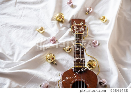 Ukulele guitar, Christmas balls and garland lights on white. Winter festive composition. Ukulele guitar, Christmas balls and garland lights on white. Winter festive composition. 96841488