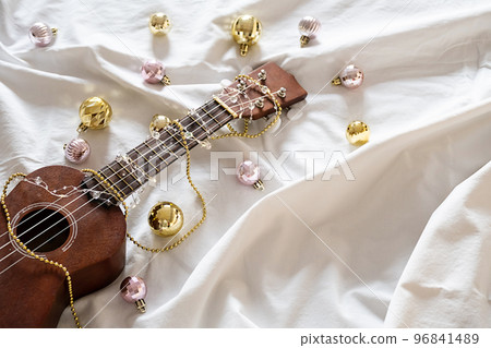 Ukulele guitar, Christmas balls and garland lights on white. Winter festive composition. Ukulele guitar, Christmas balls and garland lights on white. Winter festive composition. 96841489