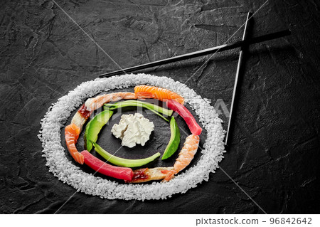 Circle of rice, salmon, eel, tuna and shrimps, avocado and cream cheese with chopsticks on black background 96842642