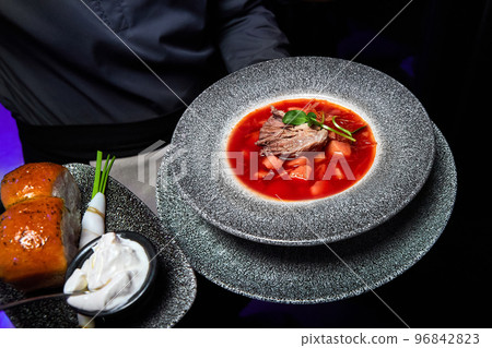 The waiter holds a plate with Borscht with veal, donuts, sour cream, onion and lard The waiter holds a plate with Borscht with veal, donuts, sour cream, onion and lard 96842823