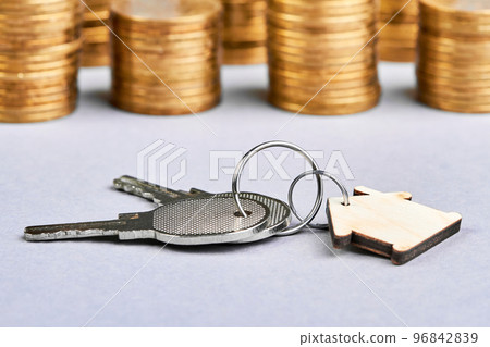 Trinket in the form of a wooden house with the keys to the apartment on the background of stacks of coins Trinket in the form of a wooden house with the keys to the apartment on the background of stacks of coins 96842839