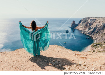 Side view a Young beautiful sensual woman with black hair in a long mint dress posing on a beach with calm sea bokeh lights on sunny day. Girl on the nature on blue sky background. Fashion photo Side view a Young beautiful sensual woman with black hair in a long mint dress posing on a beach with calm sea bokeh lights on sunny day. Girl on the nature on blue sky background. Fashion photo 96843599