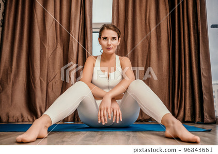 Well looking middle aged woman with long hair, fitness instructor in white sportswear, doing stretching and pilates on yoga mat at home. Healthy lifestyle, harmony, fitness yoga and meditation. Well looking middle aged woman with long hair, fitness instructor in white sportswear, doing stretching and pilates on yoga mat at home. Healthy lifestyle, harmony, fitness yoga and meditation. 96843661