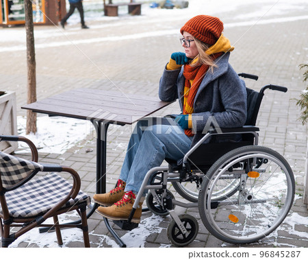 Caucasian woman in wheelchair sitting at outdoor cafe table. Caucasian woman in wheelchair sitting at outdoor cafe table. 96845287