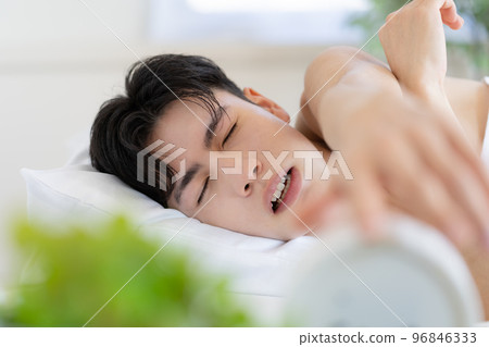 Young man waking up in bed in the morning and trying to turn off the alarm clock 96846333
