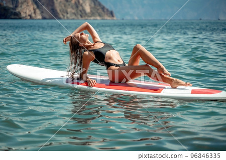 Woman sap sea. Sports girl on a surfboard in the sea on a sunny summer day. In a black bathing suit, he sits on a sapa in the sea. Rest on the sea. 96846335