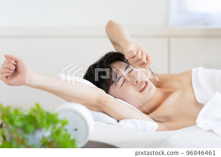 Young man waking up in bed and stretching Young man waking up in bed and stretching 96846461