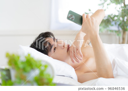 Young man watching smartphone in bed Young man watching smartphone in bed 96846536