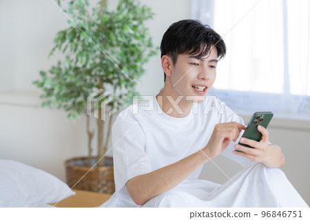 Young man getting up in bed and looking at smartphone Young man getting up in bed and looking at smartphone 96846751