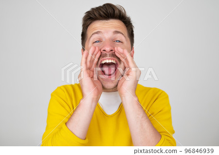 Excited young caucasian man shouting with hands cupped around mouth  96846939
