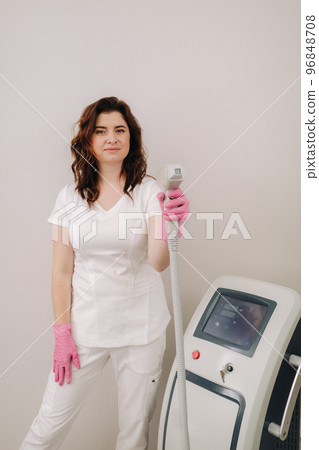 Portrait of the master of laser hair removal. A woman in a white coat holds a laser hair removal device in her hands 96848708