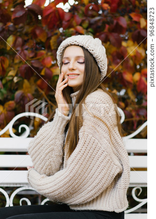 A girl in warm clothes is sitting on a bench in the autumn Park and enjoying the weather A girl in warm clothes is sitting on a bench in the autumn Park and enjoying the weather 96848723