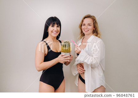 Cactus concept. Unshaven body . One girl is holding a cactus in her hands, and the second girl is holding a razor. Symbol of unshaven body parts 96848761