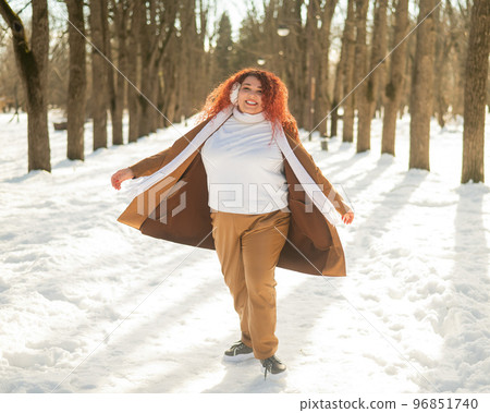 A fat woman listens to music with headphones and dances in the park in winter.  96851740