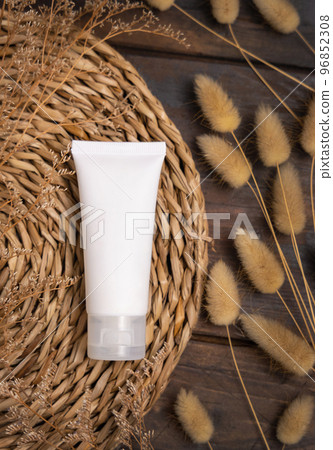 White cream tube on wattled placemat near Hare's Tail grass top view. Cosmetic Mockup 96852308