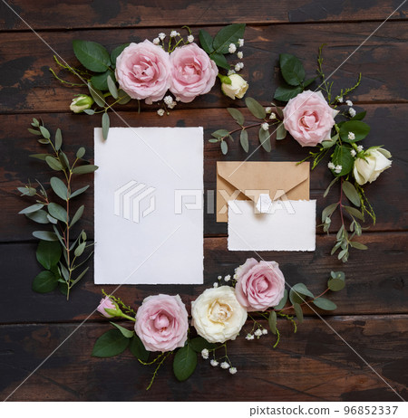 Cards and envelope between pink and cream roses on brown wood top view, wedding mockup Cards and envelope between pink and cream roses on brown wood top view, wedding mockup 96852337
