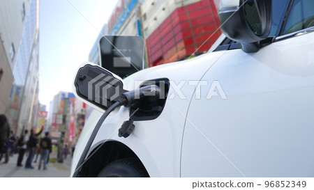 Progressive EV car charging battery from charging point in city area with people 96852349