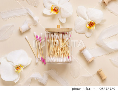 Bamboo cotton buds in a jar near white orchid flowers on light beige. Eco friendly skincare product Bamboo cotton buds in a jar near white orchid flowers on light beige. Eco friendly skincare product 96852529
