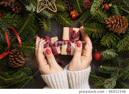 Female hands holding two gift boxes on a wooden table near Christmas decorations top view Female hands holding two gift boxes on a wooden table near Christmas decorations top view 96852546