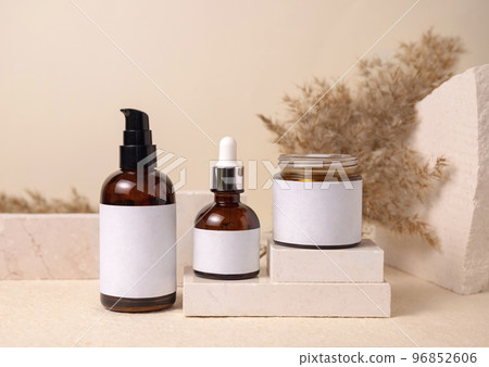 Glass bottles on travertine stone against dry pampas grass on beige close up, cosmetic mockup Glass bottles on travertine stone against dry pampas grass on beige close up, cosmetic mockup 96852606