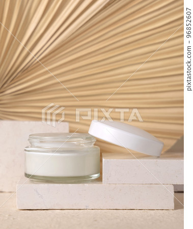 Opened cream jar on travertine stone against dry beige palm leaf close up, cosmetic mockup 96852607